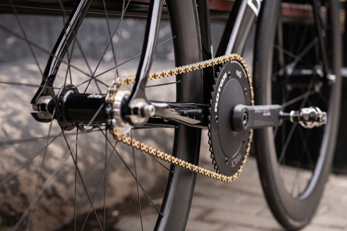 Goldene Fahrradkette am schwarzen Rennradantrieb mit Rotor-Kurbelgarnitur in der Nahaufnahme
