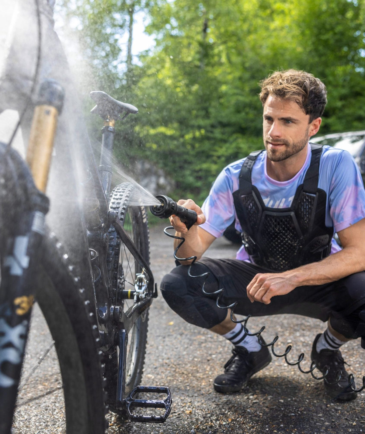 Ein Mann reinigt mit dem Kärcher OC 4 Niederdruckreiniger ein Mountainbike im Freien, während Wassernebel den Rahmen umhüllt.
